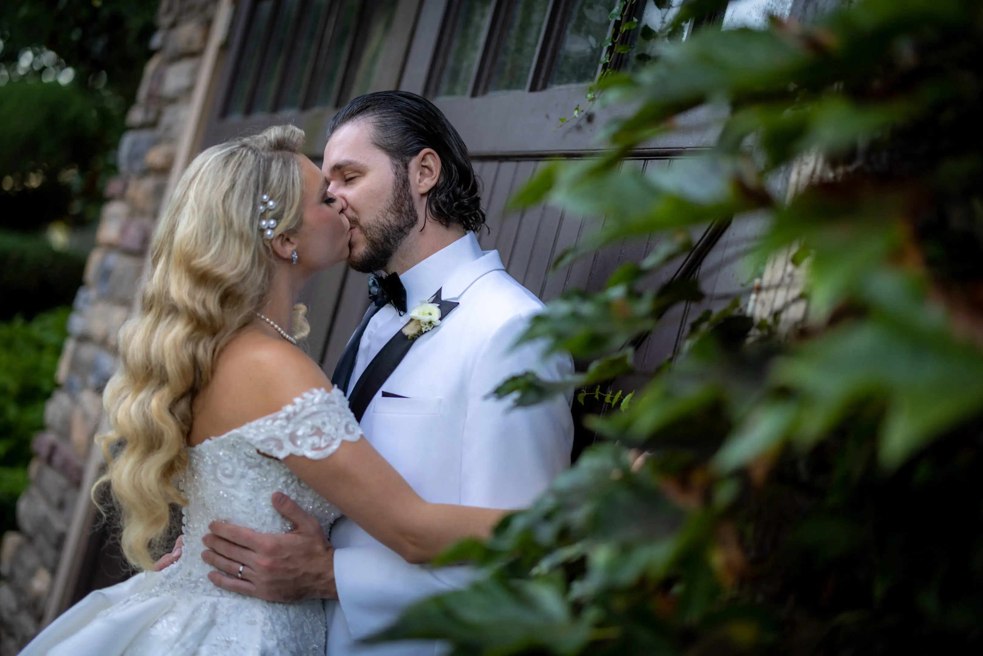 A bride and groom kissing in front of a wooden fence.